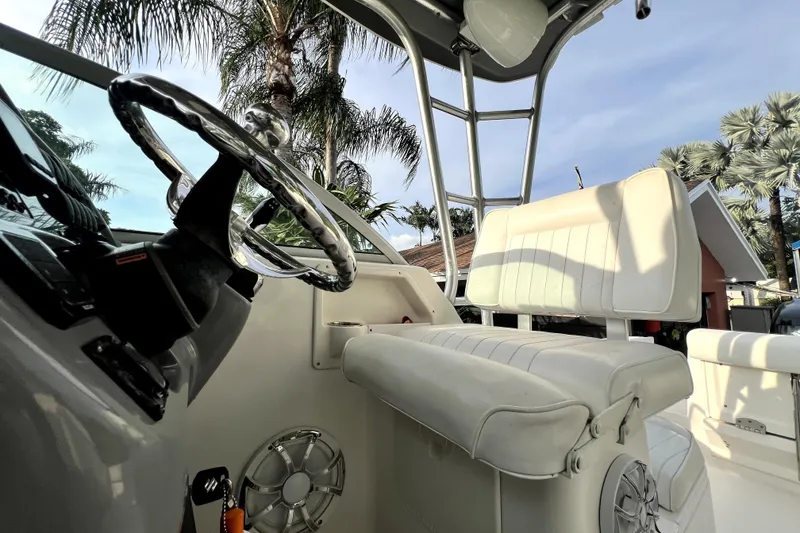 Slide: The Image of 2014 Robalo R265 Walkaround boat interior with steering wheel and seating, surrounded by palm trees. - 61