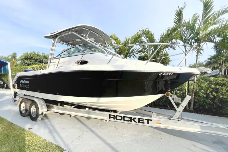 The Image of Un bateau Robalo R265 Walkaround sur une remorque, entouré de palmiers. - 0