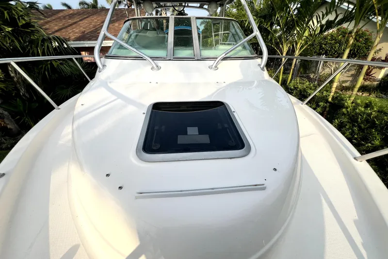 Slide: The Image of 2014 Robalo R265 Walkaround boat deck with hatch, surrounded by lush greenery. - 93