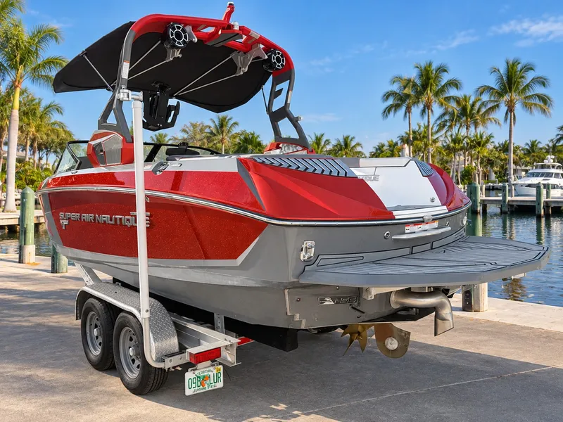 Slide: The Image of 2019 Nautique Super Air Nautique G23 in red and gray on a trailer by the water. - 1