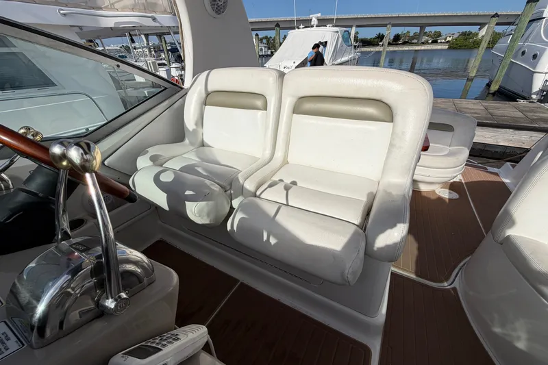 Slide: The Image of 2006 Sea Ray Sundancer 320 cockpit with white seating and control panel, docked by the water. - 49