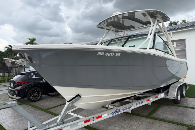Slide: The Image of 2021 Cobia 240 Dual Console boat on trailer, parked outdoors under cloudy sky. - 24