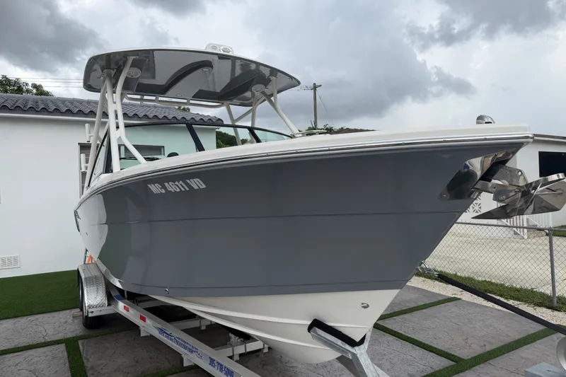 Slide: The Image of 2021 Cobia 240 Dual Console boat on trailer, parked outdoors under cloudy sky. - 25