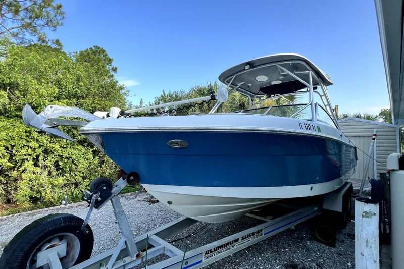 Slide: The Image of 2012 Robalo R247 Dual Console boat on trailer, blue hull, parked outdoors. - 0