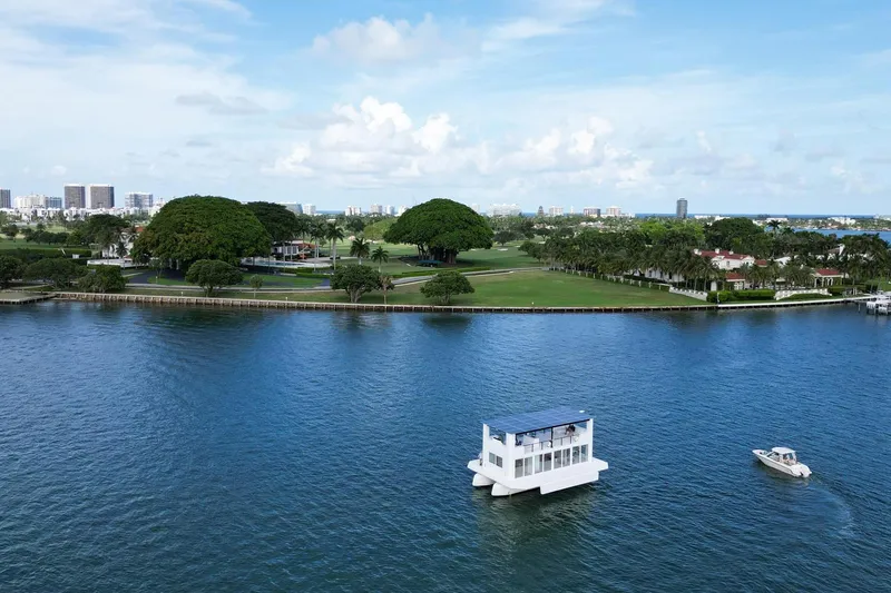 Slide: The Image of Floating Arkhaus Villa 50 on serene water with lush greenery and cityscape in the background, 2025. - 1