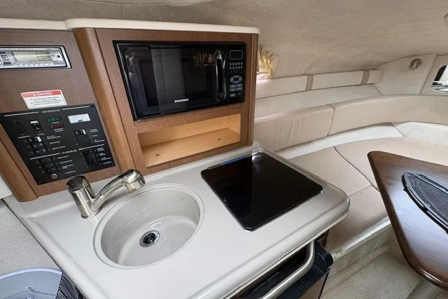Slide: The Image of 2013 Sea Ray 240 Sundancer cabin with kitchenette, featuring sink, microwave, and stove. - 16