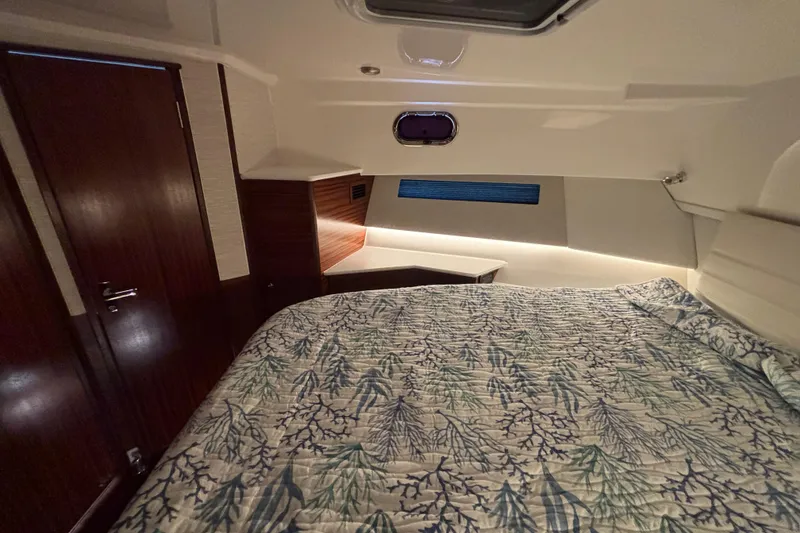 Slide: The Image of 2024 Pursuit OS 445 Offshore cabin with bed, wood accents, and ambient lighting. - 102
