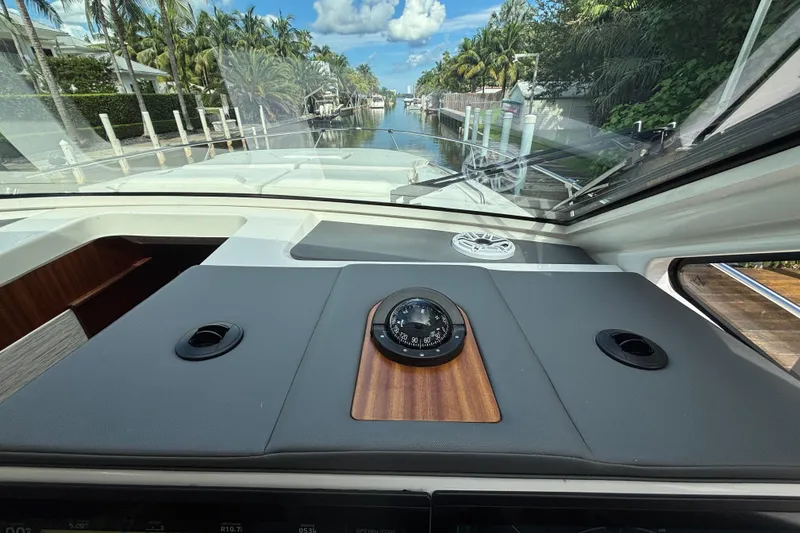 Slide: The Image of 2024 Pursuit OS 445 Offshore boat interior with compass, docked in a scenic canal. - 78