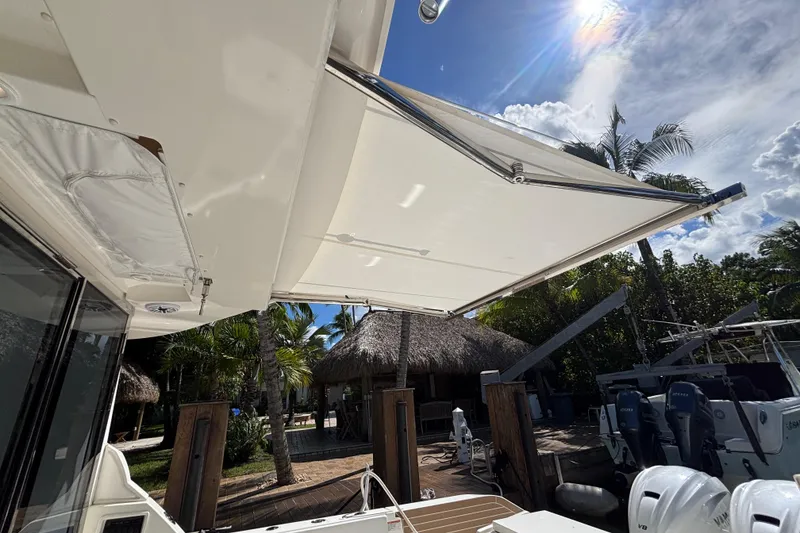 Slide: The Image of 2024 Pursuit OS 445 Offshore boat with extended sunshade, docked under a sunny sky. - 51