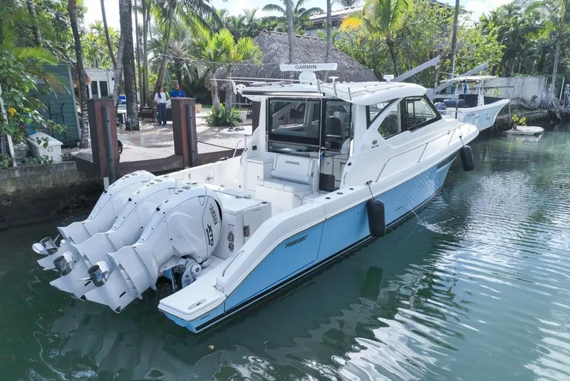 Slide: The Image of 2024 Pursuit OS 445 Offshore boat docked in a tropical setting with triple outboard engines. - 8
