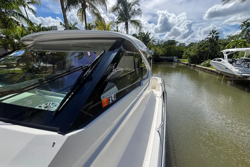 Slide: The Image of 2024 Pursuit OS 445 Offshore boat docked on a serene canal, surrounded by lush palm trees. - 37