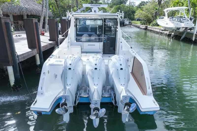 Slide: The Image of 2024 Pursuit OS 445 Offshore boat with triple outboard engines docked in a serene canal. - 12
