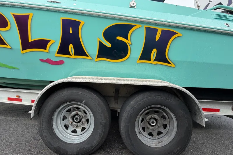 Slide: The Image of Colorful Apache 28 Splash boat on trailer, showcasing vibrant lettering and sturdy wheels. - 103