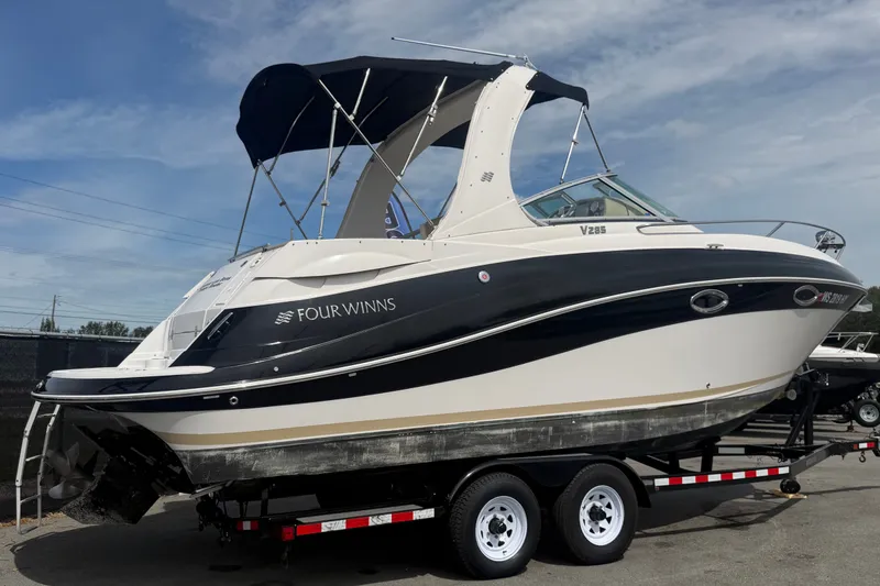 Slide: The Image of 2011 Four Winns V285 boat on trailer, featuring sleek design and canopy under blue sky. - 2