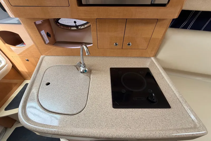 Slide: The Image of 2011 Four Winns V285 boat kitchen with sink and stovetop, featuring wood cabinetry. - 62