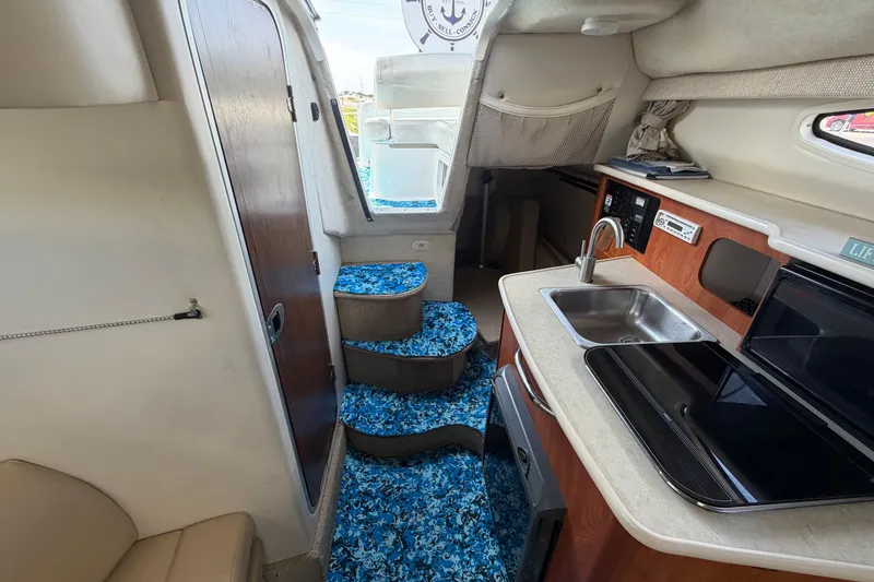 Slide: The Image of Interior of 2004 Bayliner 2452 Ciera Express, featuring kitchenette and blue-patterned flooring. - 58