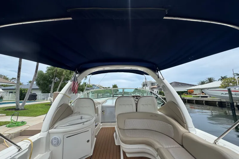 Slide: The Image of 2004 Sea Ray 340 Sundancer interior with seating and canopy, docked by waterfront homes. - 11