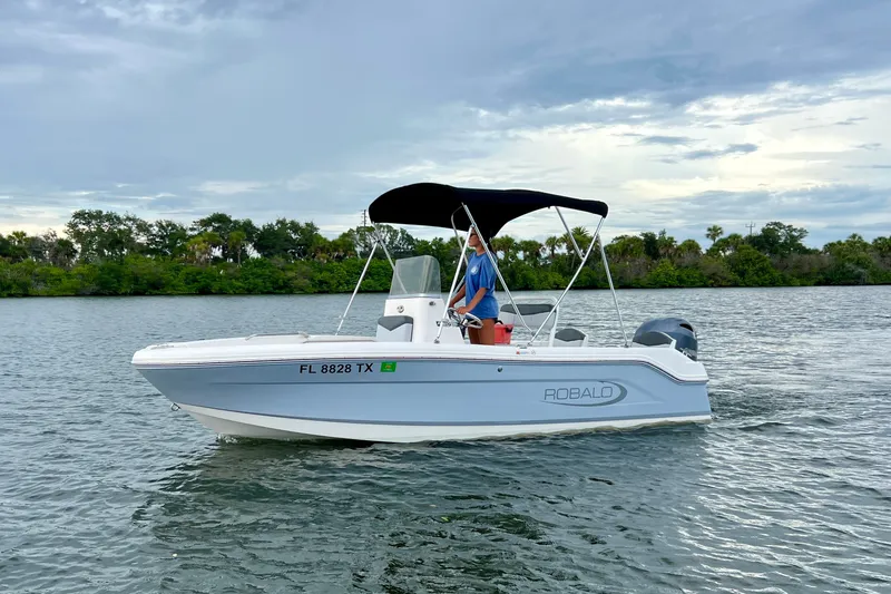 Slide: The Image of 2025 Robalo R160 Center Console boat on calm water with canopy and driver. - 1