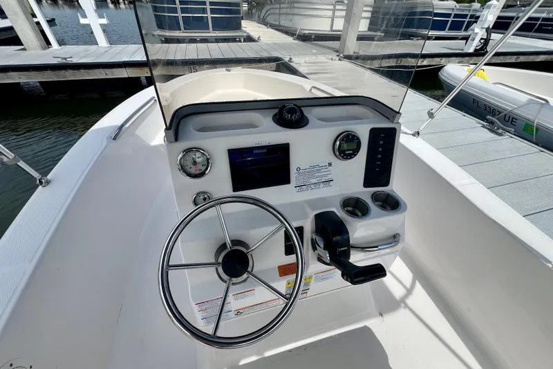 Slide: The Image of 2025 Robalo R160 Center Console boat dashboard with steering wheel and controls at marina. - 8