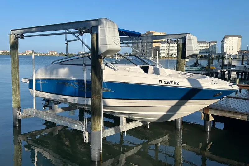 The Image of Een Regal 2400 Bowrider uit 2009 staat op een bootlift boven het water. Gebouwen op de achtergrond. - 0