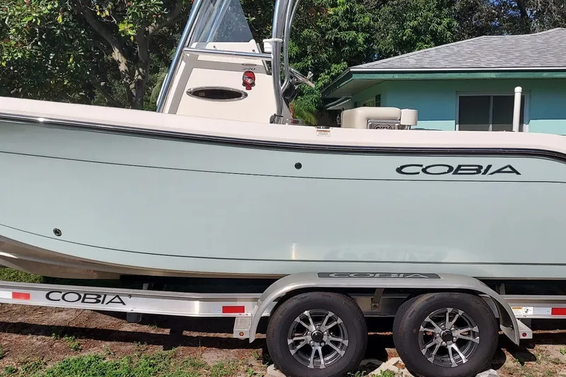 Slide: The Image of 2018 Cobia 220 Center Console boat on trailer, parked outdoors near a house. - 2