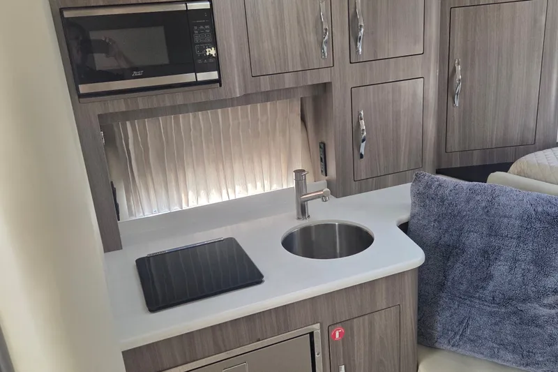 Slide: The Image of 2022 Regal 33 Express boat interior kitchen with sink, microwave, and storage cabinets. - 25