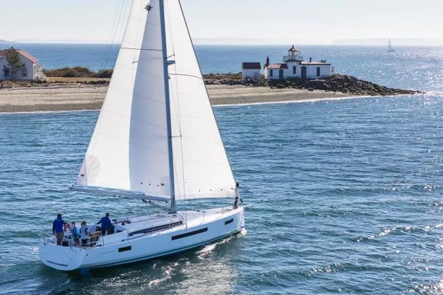 Slide: The Image of Die Jeanneau Sun Odyssey 490 segelt nahe einer Küste mit einem Leuchtturm im Hintergrund. - 25