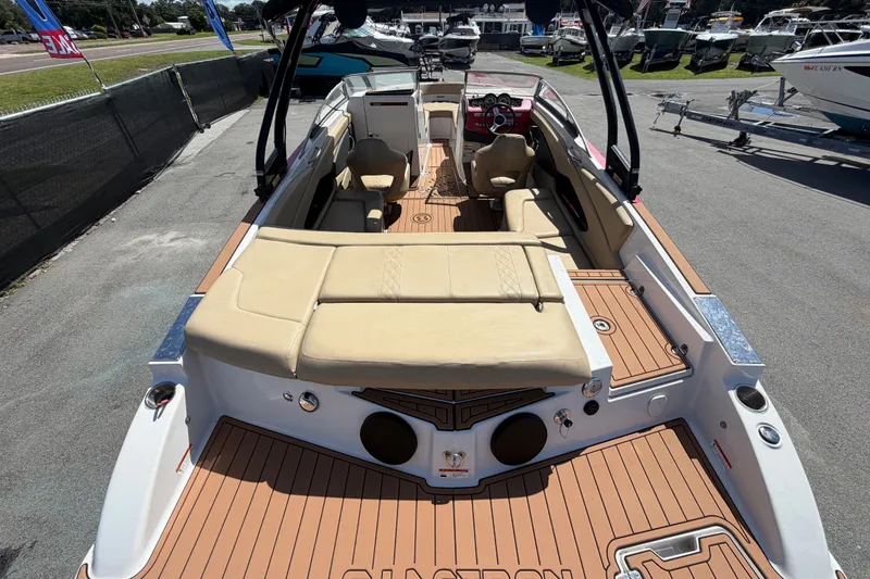 Slide: The Image of 2016 Glastron GT 245 boat with tan seating and wood-style deck, parked outdoors. - 11