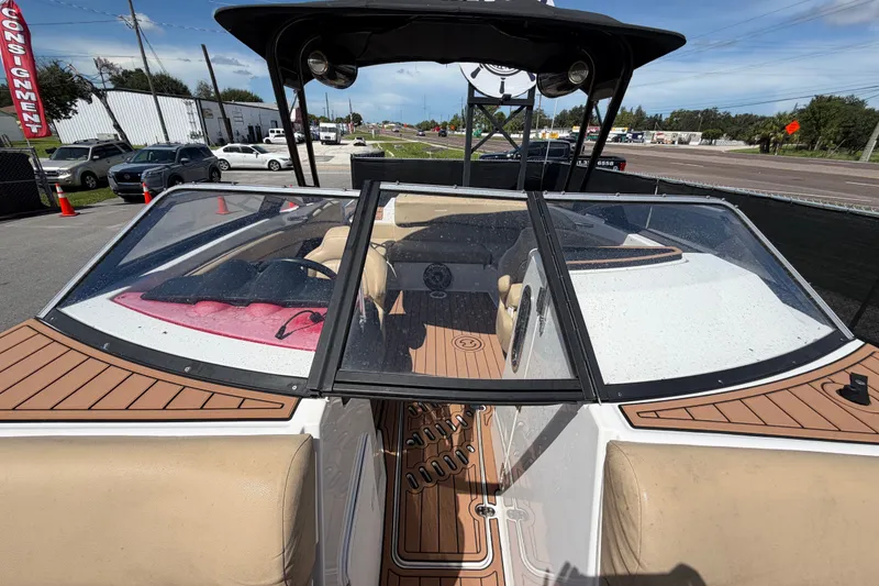 Slide: The Image of 2016 Glastron GT 245 boat interior with tan seating and wood accents, parked outdoors. - 57