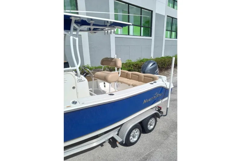 Slide: The Image of 2019 NauticStar 2102 Legacy boat on trailer, blue hull, beige seating, parked near building. - 10