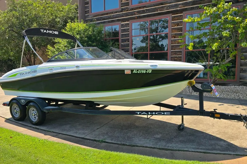 Slide: The Image of 2018 Tahoe 700 boat on trailer, parked outdoors near a building with greenery. - 4
