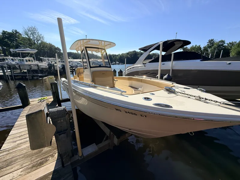 Slide: The Image of A 2018 Scout 235 XSF boat docked. It features a cream-colored deck and a T-top. - 23
