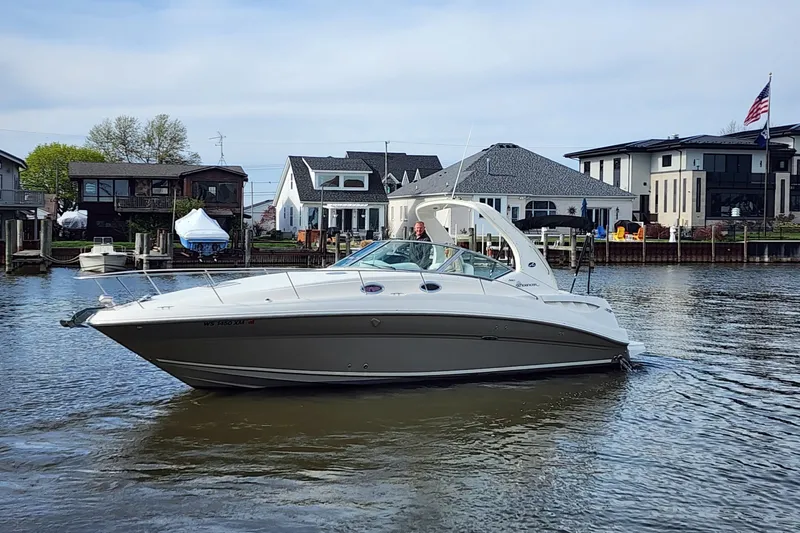 The Image of 2007 Sea Ray Sundancer 320 cruising on a calm waterfront near modern homes. - 0