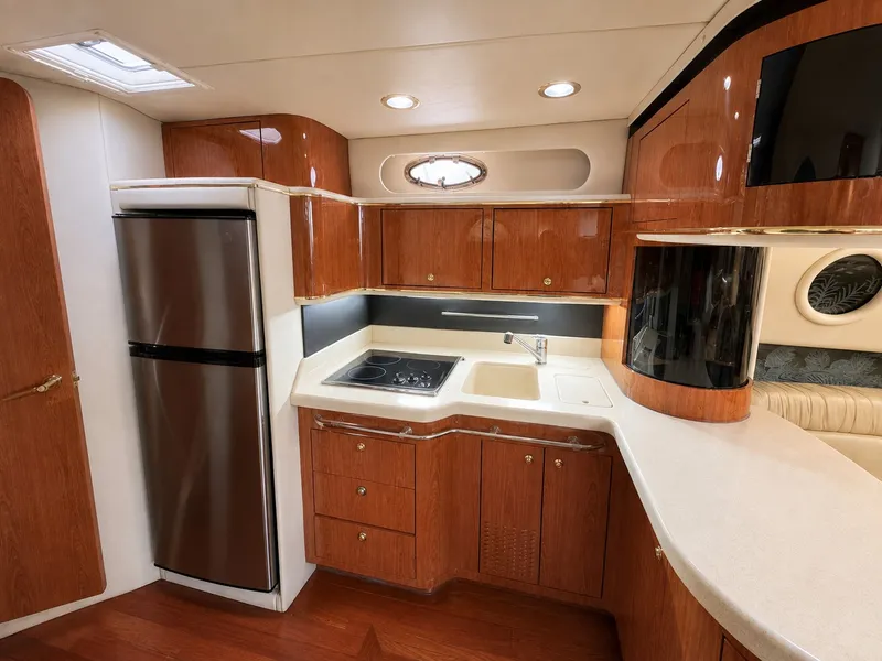 Slide: The Image of The 1999 Sea Ray 500 Sundancer's kitchen features wood cabinets, a stove, and a refrigerator. - 23