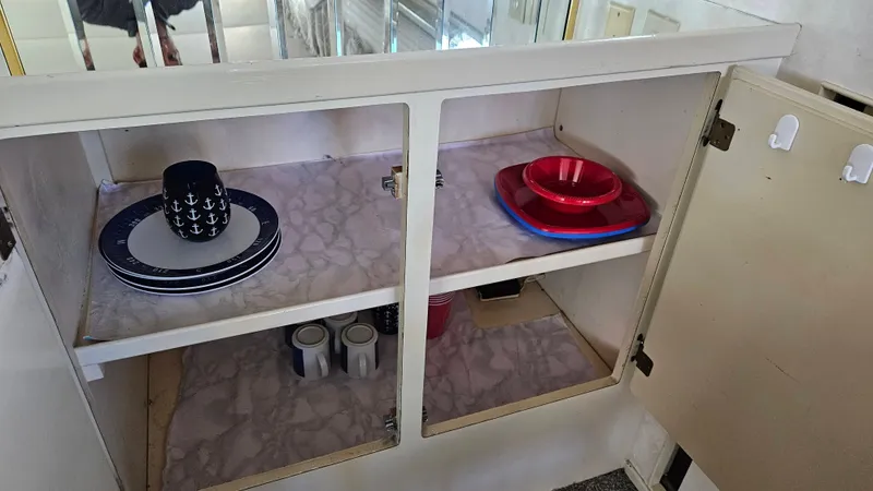 Slide: The Image of An open cabinet with dishes, including plates and mugs, inside a boat. - 26