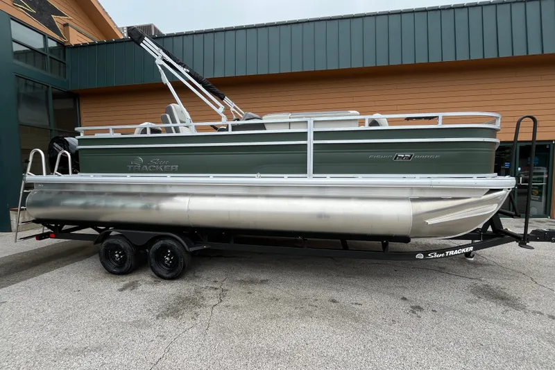 The Image of 2027 Sun Tracker Fishin' Barge 22 DLX pontoon boat on trailer, parked outdoors. - 0