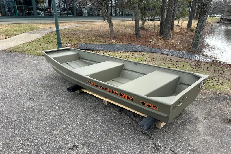 The Image of 2027 Tracker Grizzly 12 Jon boat on pavement near a pond and trees. - 0