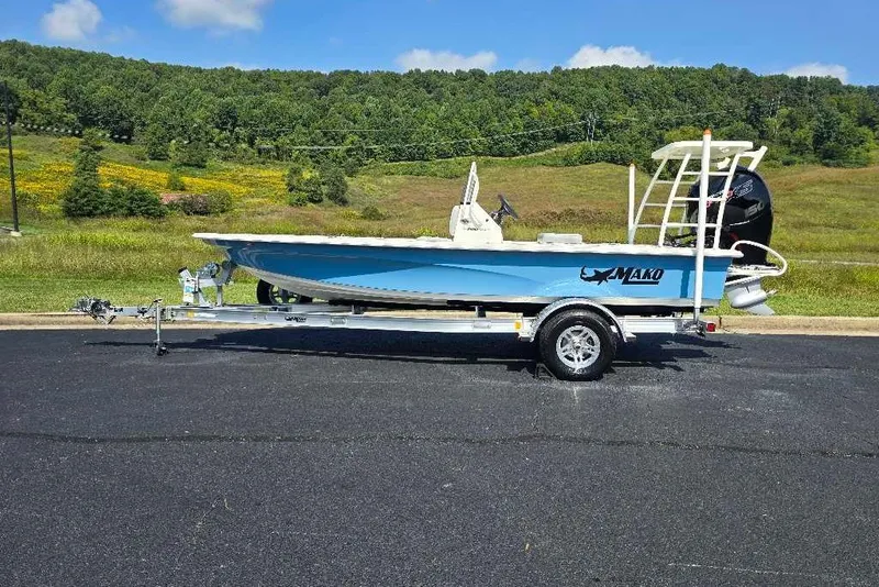 Slide: The Image of 2026 Mako 18 Pro Skiff boat on trailer, parked on asphalt with scenic green landscape. - 2