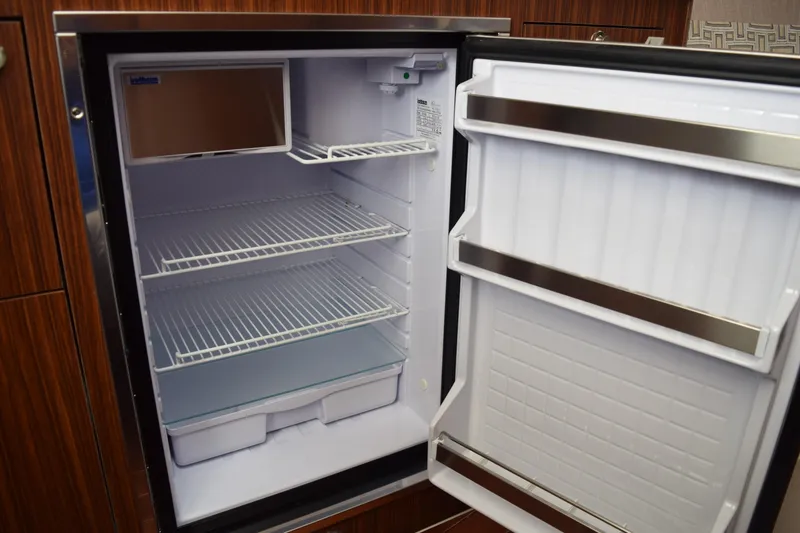 Slide: The Image of 2022 Pursuit OS 355 Offshore boat refrigerator, open with empty shelves and door storage. - 420