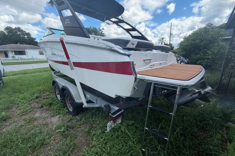 Slide: The Image of 2022 Regal LS2 boat on trailer with swim platform and ladder, parked on grass. - 2
