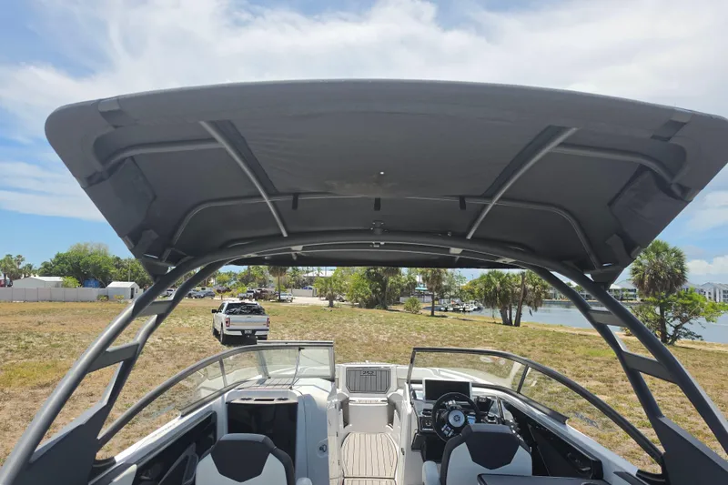 Slide: The Image of 2022 Yamaha Boats 252SD interior with canopy, parked near a scenic waterfront. - 70