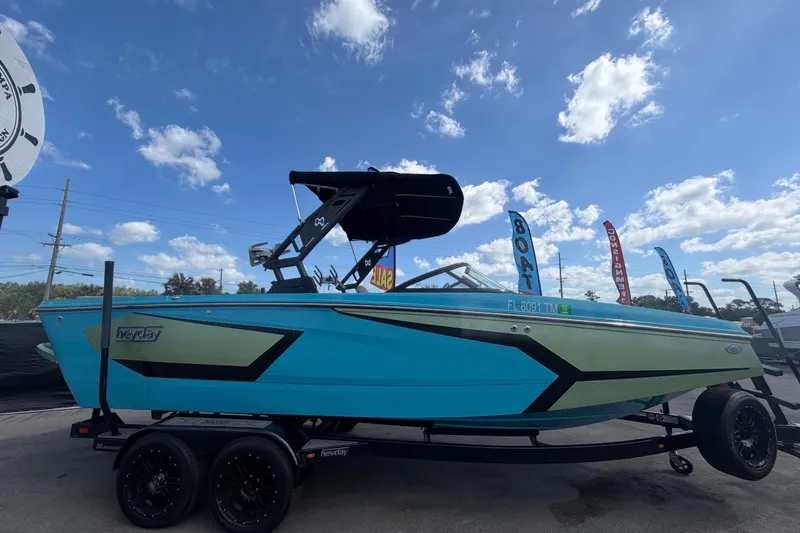 Slide: The Image of 2023 Heyday WTSurf boat in vibrant blue and green, displayed outdoors under a clear sky. - 1