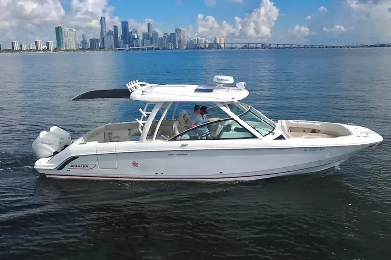 Slide: The Image of 2021 Boston Whaler 320 Vantage cruising on calm waters with city skyline backdrop. - 2