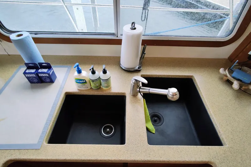 Slide: The Image of A kitchenette with two sinks, cleaning supplies, and a window overlooking the water. - 30