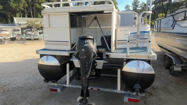 Slide: The Image of A 2008 Manitou OASIS 20 pontoon boat with an outboard motor, parked on a trailer. - 2