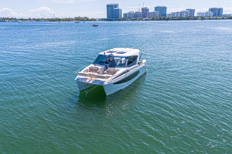 Slide: The Image of 2024 Aquila 36 Sport boat cruising on a sunny day with city skyline backdrop. - 10