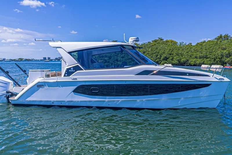 Slide: The Image of 2024 Aquila 36 Sport boat on water, sleek design, sunny day, lush greenery background. - 3