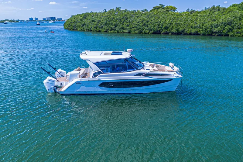 Slide: The Image of 2024 Aquila 36 Sport yacht cruising on clear blue water near lush green shoreline. - 11