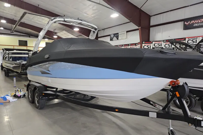 Slide: The Image of 2025 Monterey M-22 boat in showroom, covered and on trailer, with sleek blue and white design. - 2