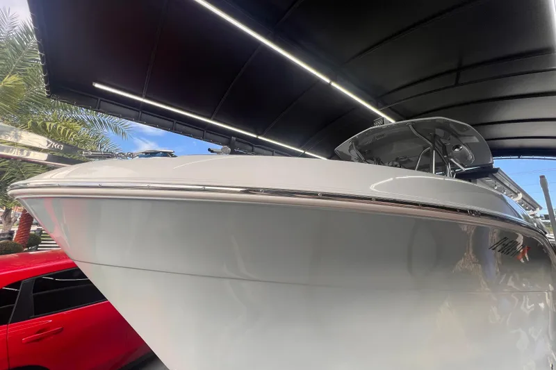 Slide: The Image of 2022 Aquasport 2300 Center Console boat under a canopy, with a red car nearby. - 1